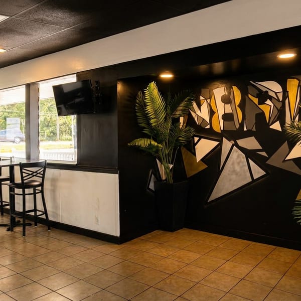 Modern restaurant interior with high-top tables, large windows, and a geometric mural on a black wall.