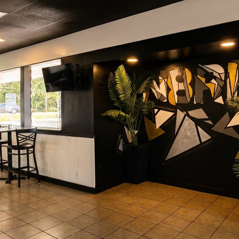 Modern restaurant interior with high-top tables, large windows, and a geometric mural on a black wall.