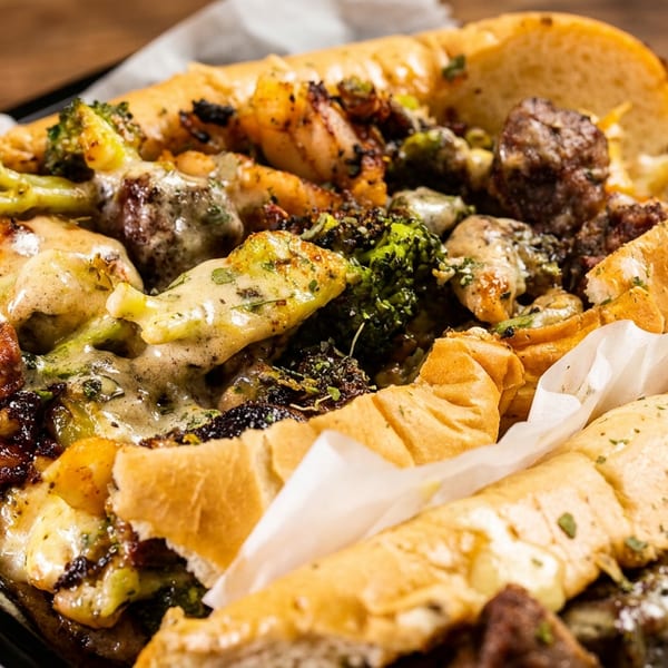 Cheesy steak and broccoli sub sandwich in a black tray on a wooden table.