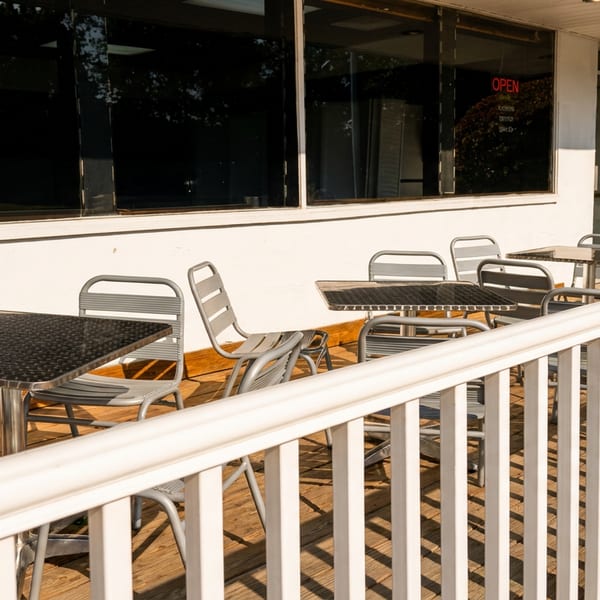 Outdoor patio with gray metal tables and chairs on a wooden deck next to a white building.