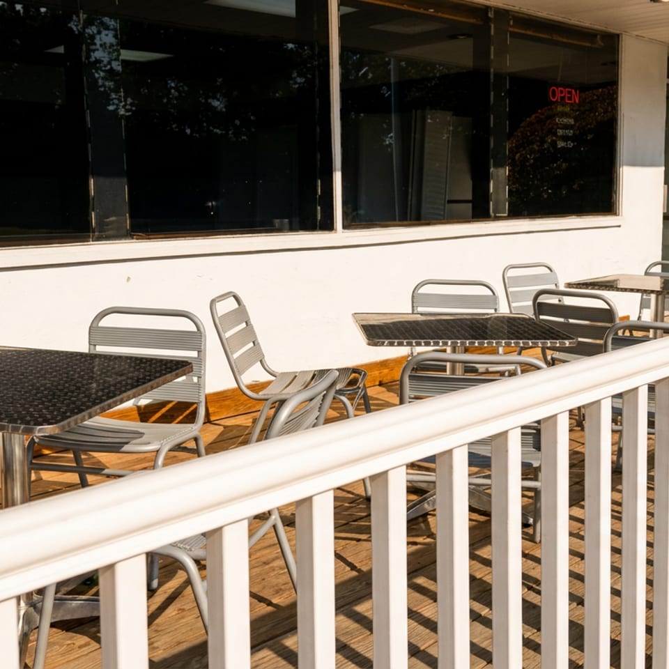 Outdoor patio with gray metal tables and chairs on a wooden deck next to a white building.
