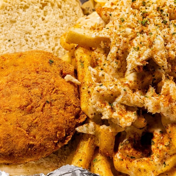 Fried chicken sandwich with seasoned fries and crab meat in a takeout container.
